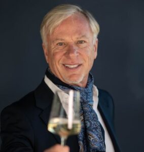 Smiling elderly man holding a glass of white wine.