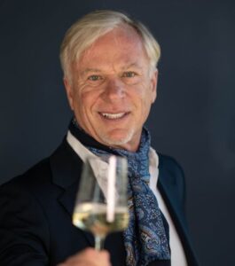 Elderly man smiling with a glass of white wine.